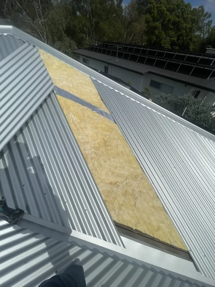 Metal roof sheets twisted out to reveal the yellow foil-backed anticon glasswool blanket beneath, exposed during an insulation upgrade