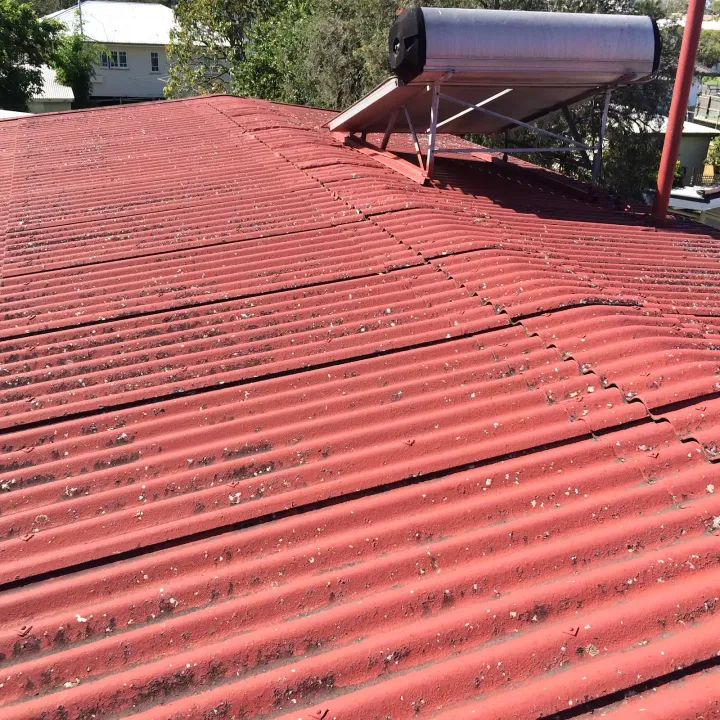 A red-painted corrugated fibro Super-6 roof seen from a distance in daylight with a rooftop solar hot-water tank, identification shot of a hard roof type