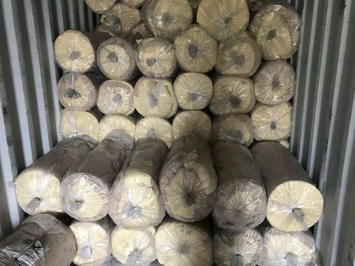 Plastic-wrapped rolls of new glasswool insulation stacked in rows inside a steel shipping container