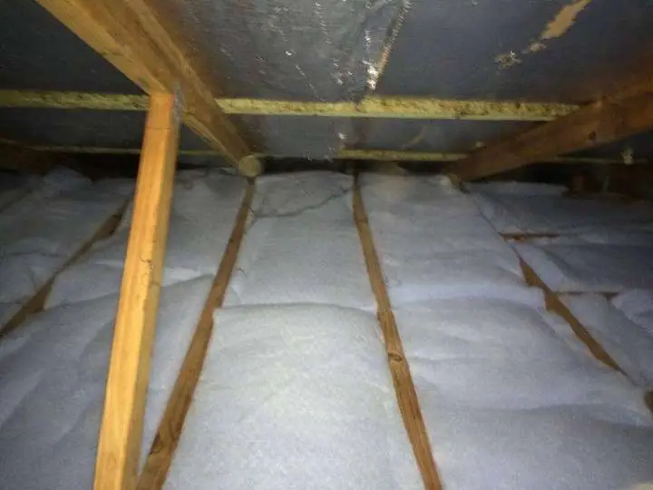 Bright white polyester batts laid neatly wall-to-wall between ceiling joists under a metal roof, Comfort Zone install