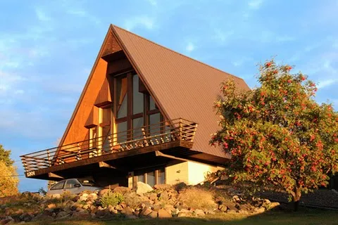 A timber A-frame house with a steep pitched metal roof and a cantilevered balcony