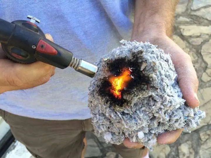 Peter holding a ball of grey cellulose in his bare hand while an oxy torch chars and glows a black crater in the middle, his hand unharmed, showing the borate-treated fibre resists flame