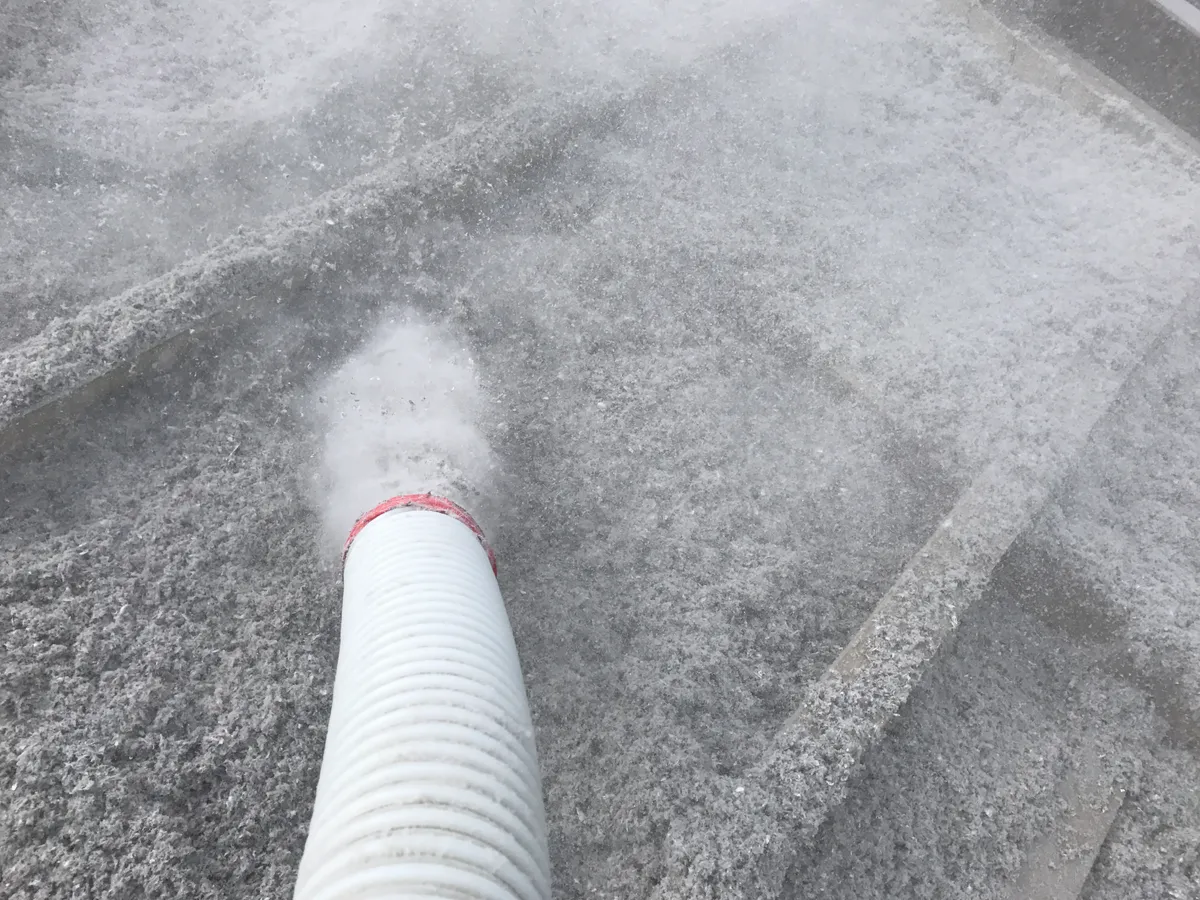 Grey cellulose fibre insulation blowing out of the Comfort Zone installer's white blower hose into a ceiling cavity, laying down as one seamless blanket