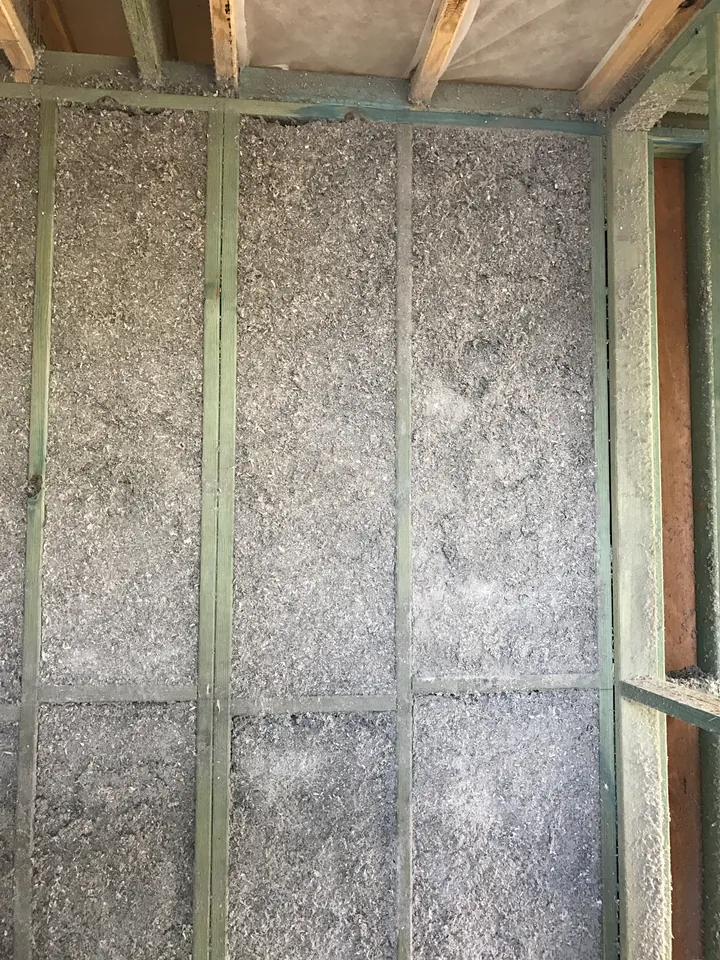 Grey cellulose fibre packed densely between timber wall studs for soundproofing during construction, Comfort Zone