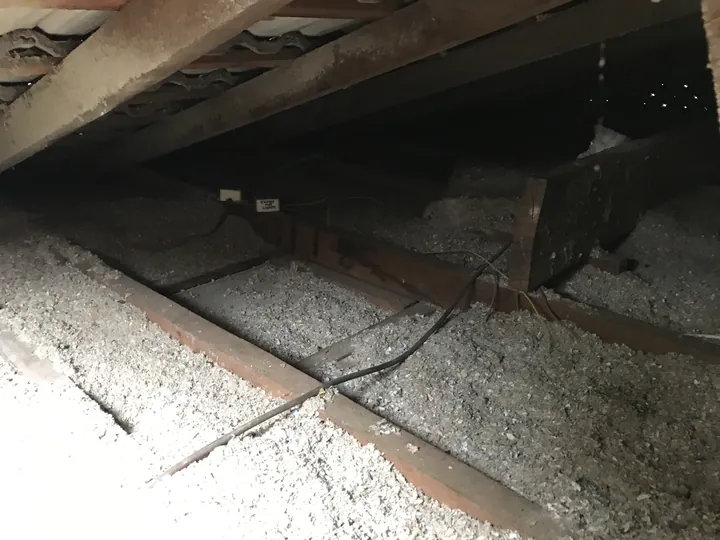 A competitor's loose cellulose laid through a dark tile-roof cavity with no protective shroud detailing around the access. Comfort Zone always shrouds the manhole