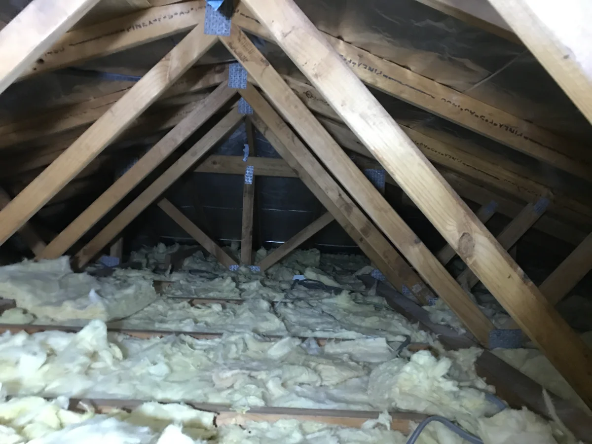 Rhino fibreglass batts laid loosely and unevenly across the ceiling joists in this garage, with gaps between sections and batts pushed up against the rafters instead of sitting flat — gaps like these are what ruin a ceiling's insulation, not the R-number on the bag.