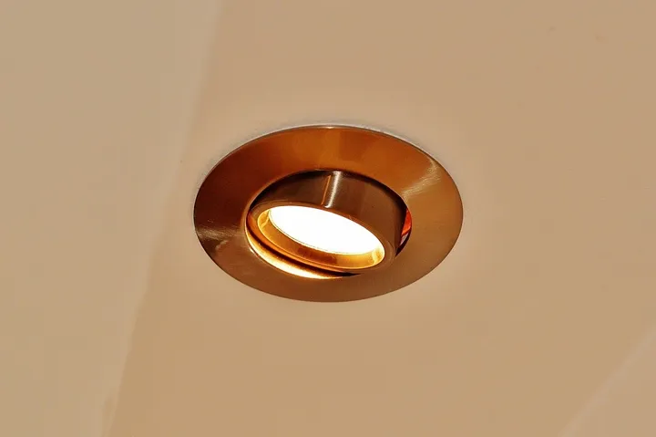 A round recessed downlight with a brushed metal trim glowing warm in an off-white ceiling