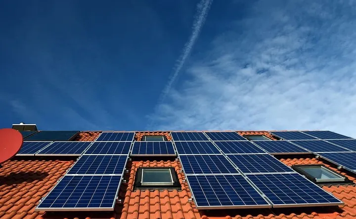 Solar panels mounted across a tiled roof, viewed from below against a blue sky