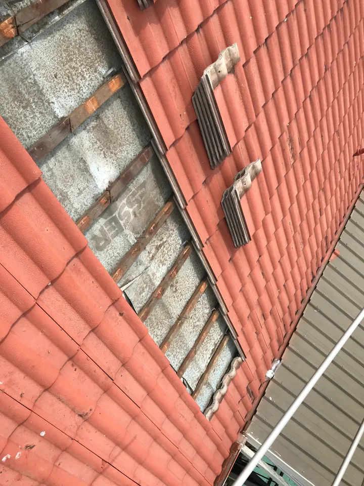 A terracotta tiled roof with a section of tiles lifted off and stacked aside, exposing the timber battens and the grey cellulose blanket sitting evenly beneath them.