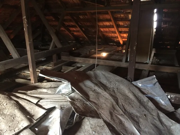 FOIL insulation (not fibreglass): old crumpled silver foil sheets torn out and strewn across a dark roof cavity with loose debris, the kind of foil we remove and dispose of