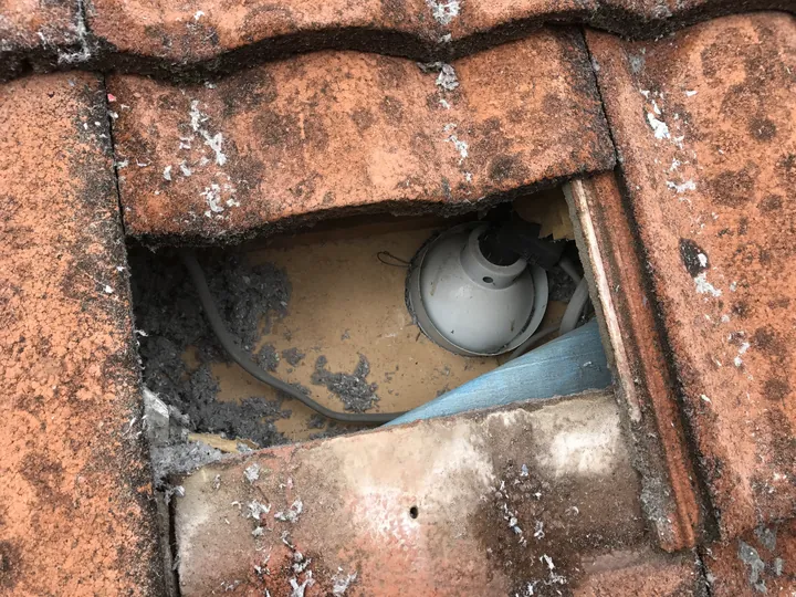 A roof tile lifted to reveal a downlight fitting and cabling in the cavity below, located before cellulose is pumped around it, Comfort Zone