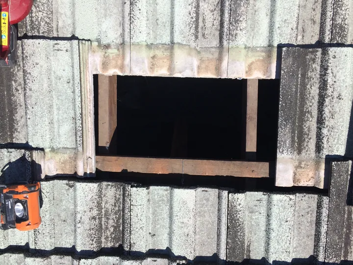 A neat access opening cut into a concrete-tile roof — three tiles slid up and two lifted out — the way Comfort Zone gets into a sealed tile roof that has no manhole