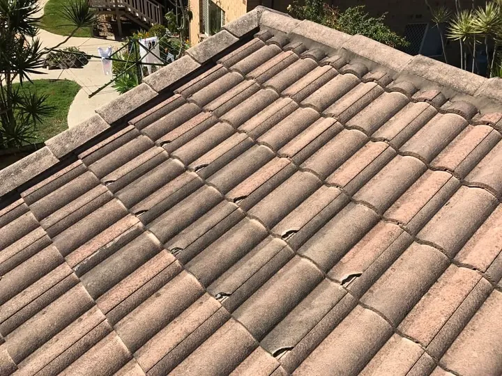 A concrete tile roof with several cracked and chipped tiles grouped toward the back, broken by another contractor and left out of sight