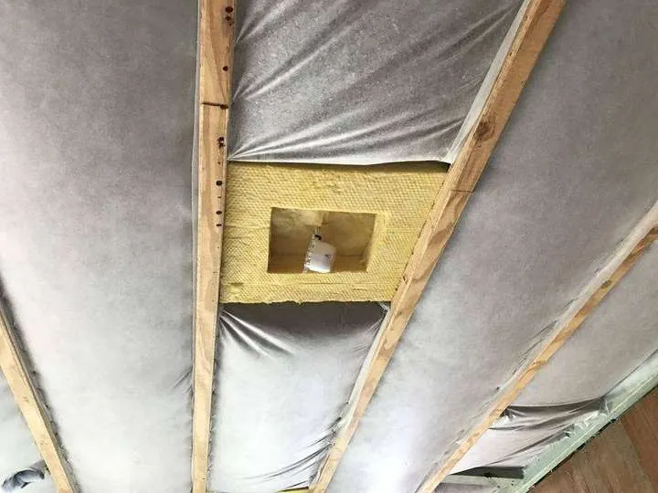 Grey sound-insulation matting stapled between the floor joists of a two-storey home, with a batt patch fitted around a downlight box, Comfort Zone