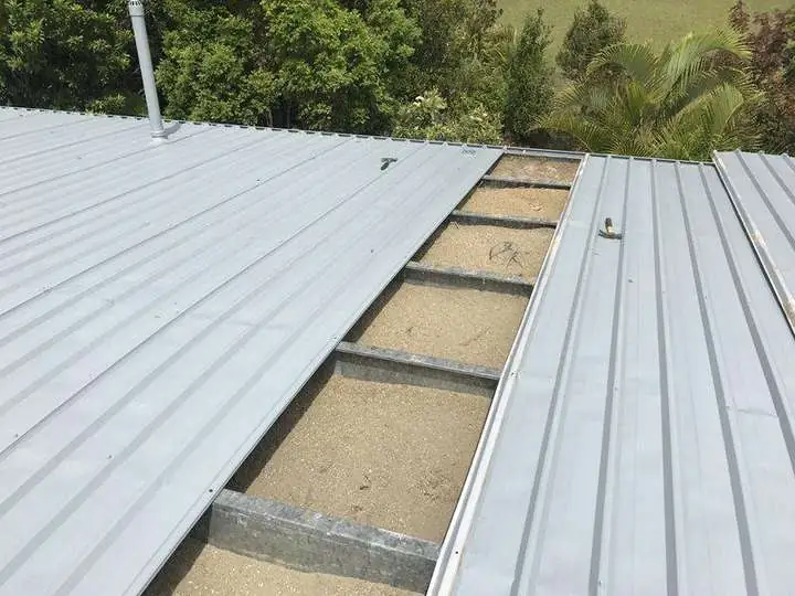 A trim-deck metal roof opened mid-job showing cellulose insulation packed between the steel battens, Comfort Zone
