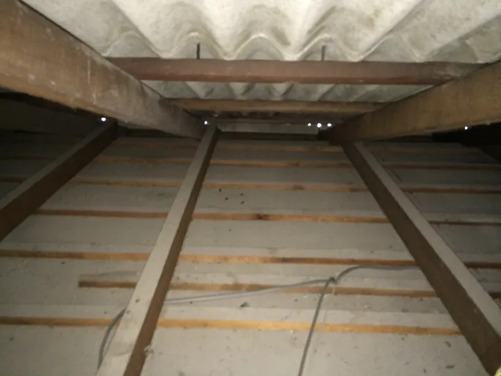 Underside of a Super-6 fibro roof showing timber battens running below the joists that hold batts off the ceiling, roof-cavity view