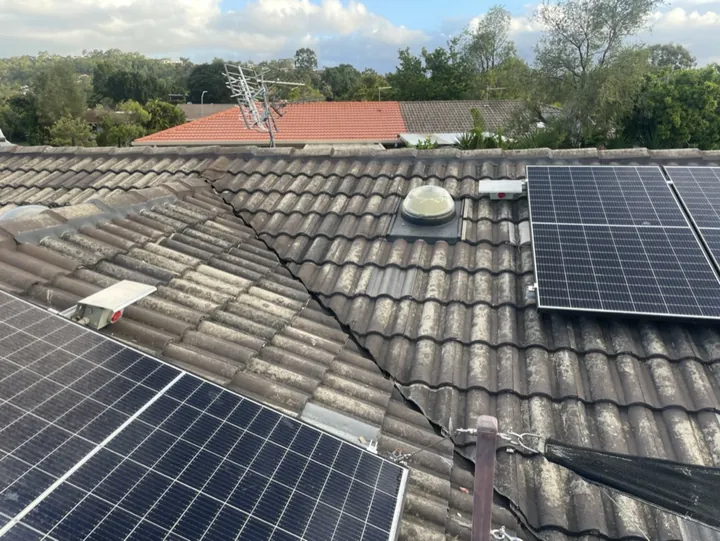A weathered concrete-tile roof eroded back to bare cement, its surface glaze worn away, fitted with solar panels and a domed skylight