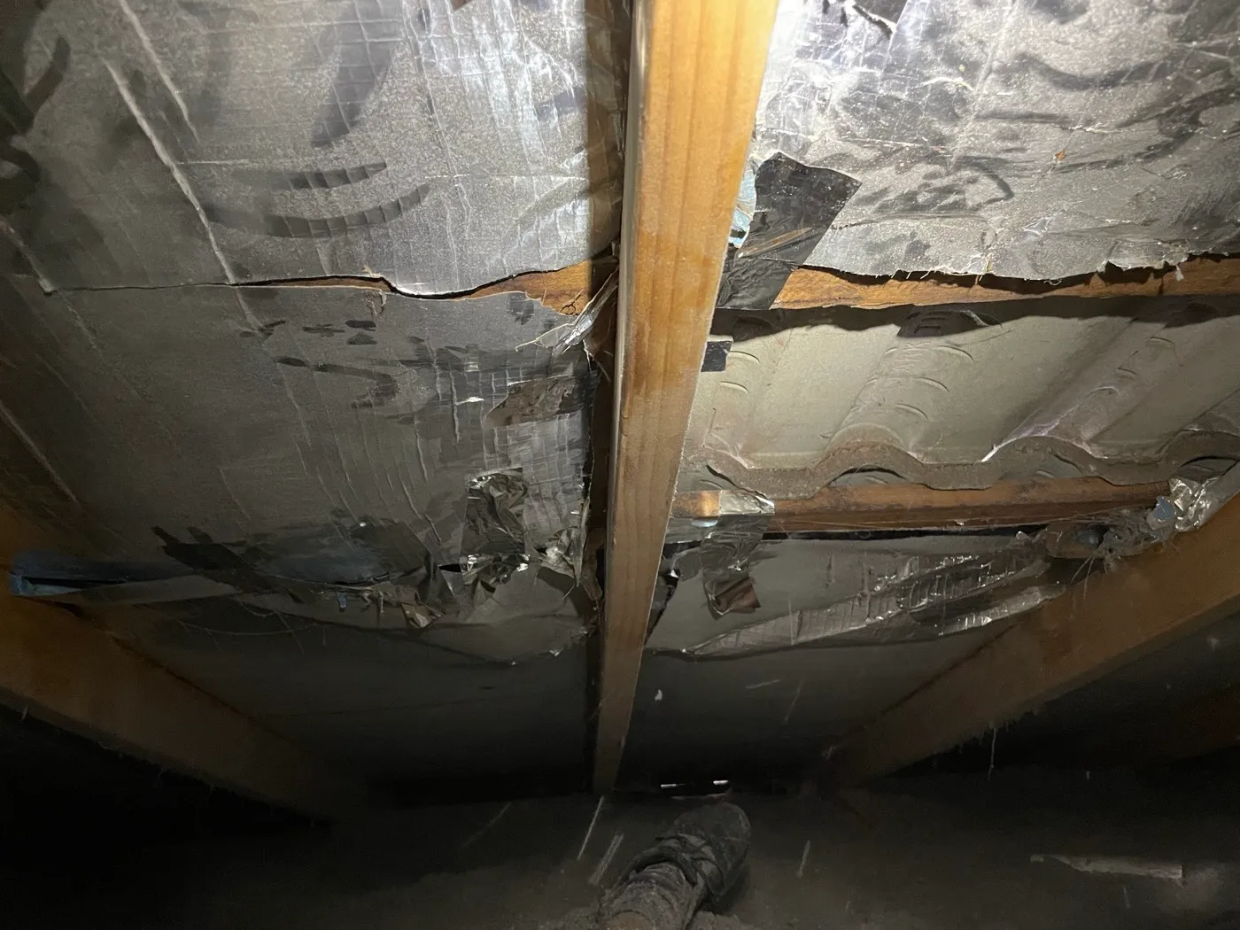 Old silver reflective foil insulation hanging in torn, shredded tatters, failed and sagging away inside the roof — Tweed Heads