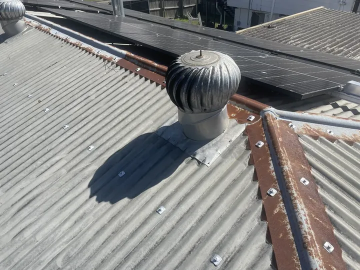 A seized, weathered whirlybird vent with its worn central spindle bored up through the dome on an old grey corrugated metal roof